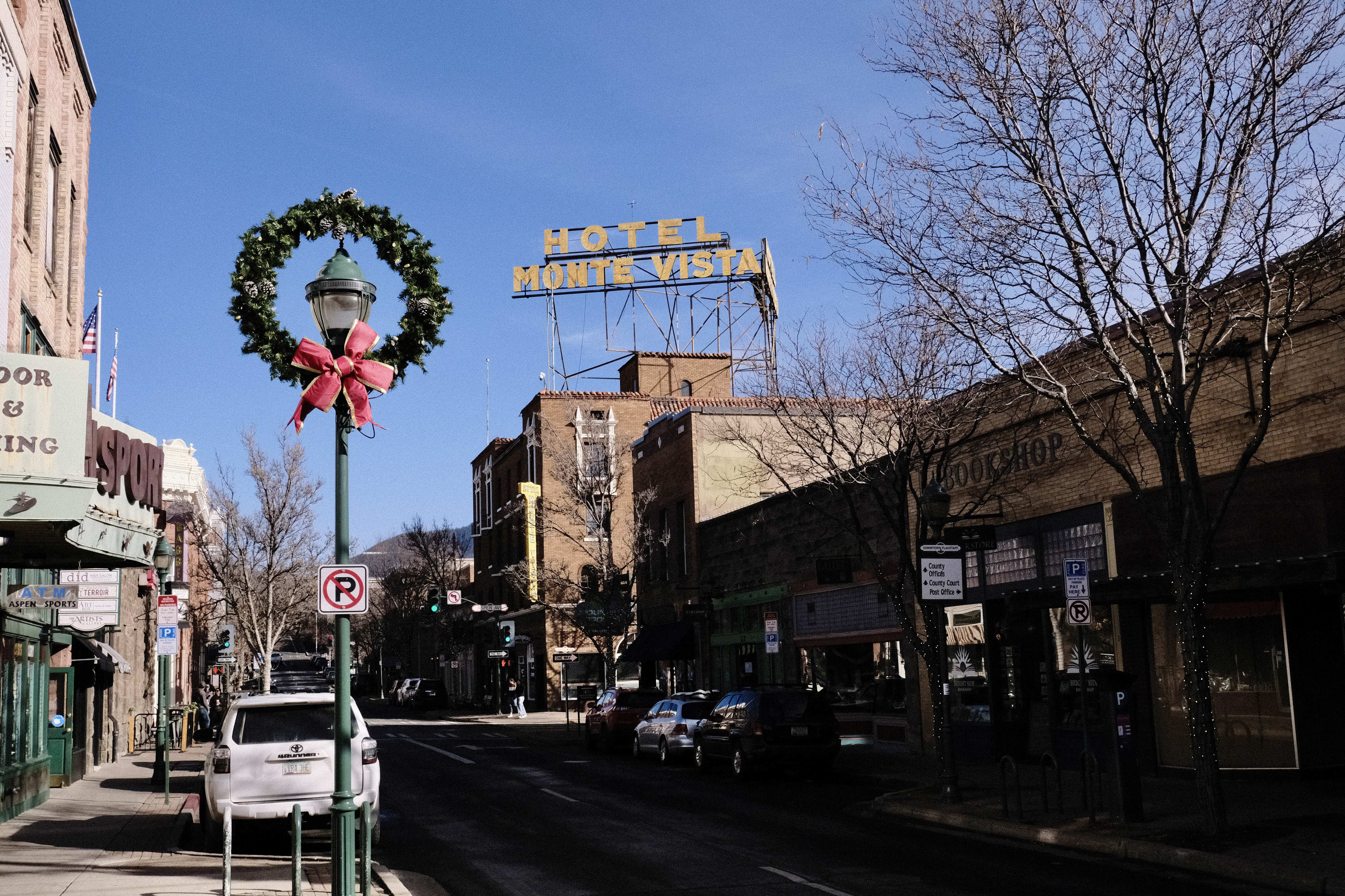looking up a street sided by brick buildings, to see a large green and red wreath, and the sign for the Hotel Monte Vista high above the street 