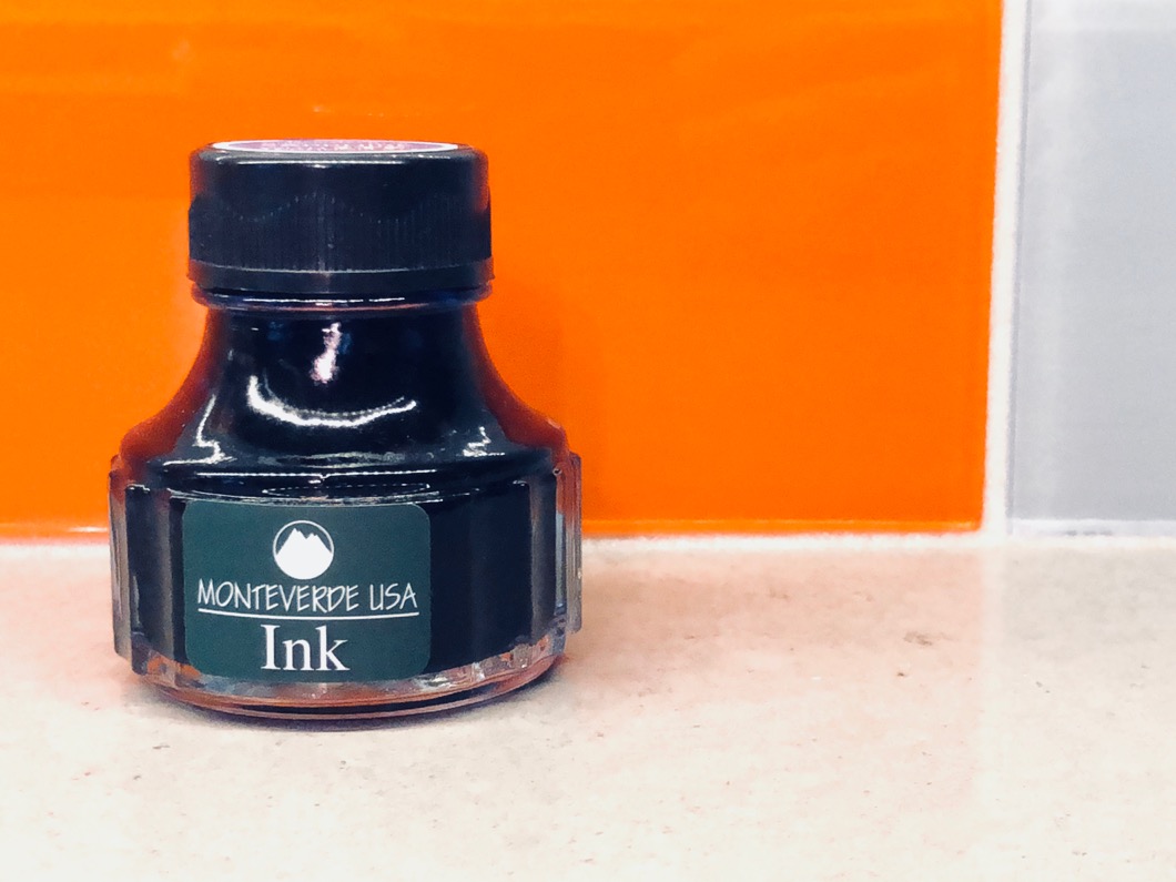 Dark blue bottle of ink on a kitchen counter with orange tile behind it.  