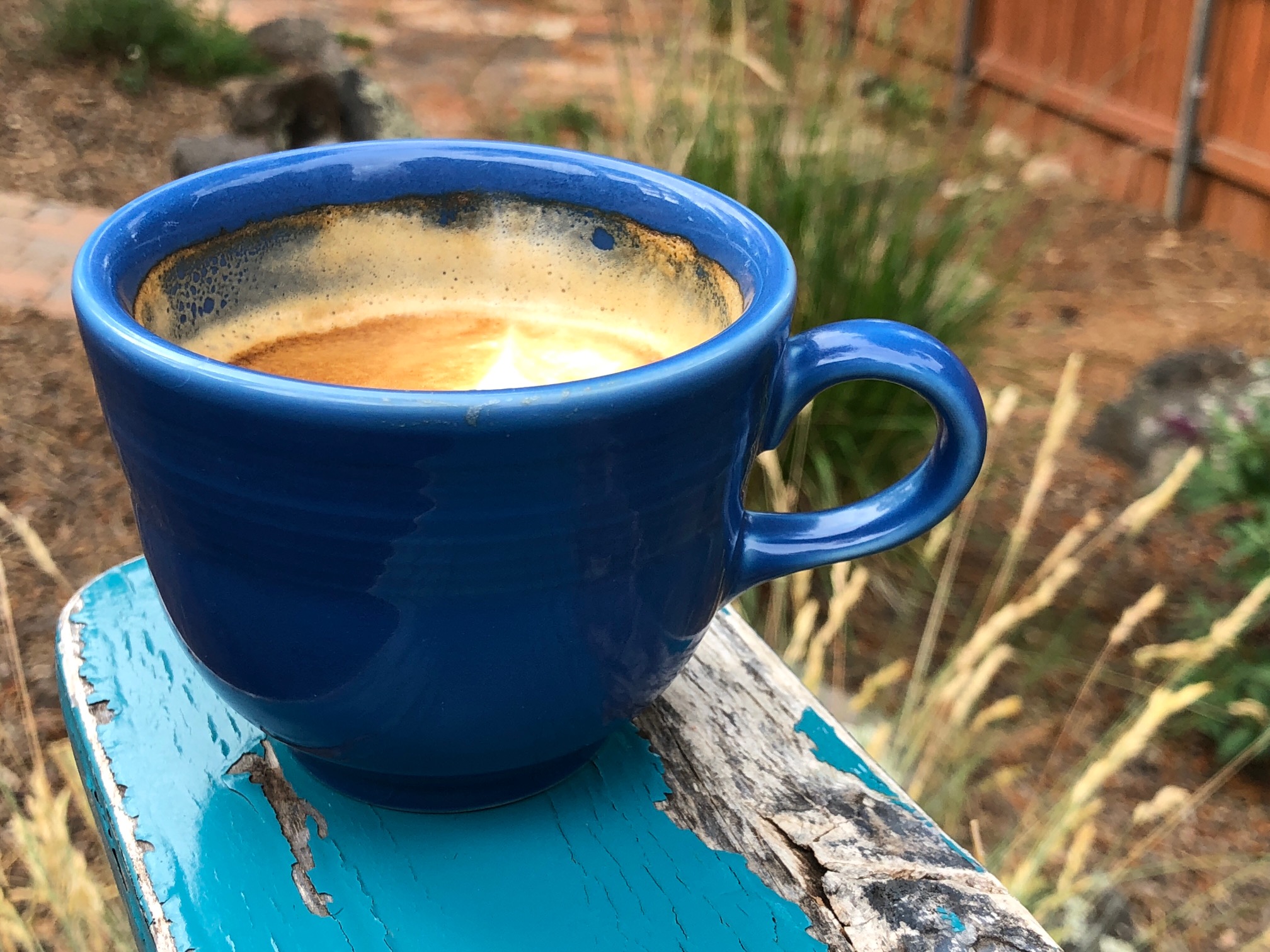 Photo of a blue cappuccino cup on a worn blue armrest of an outdoor chair.  
