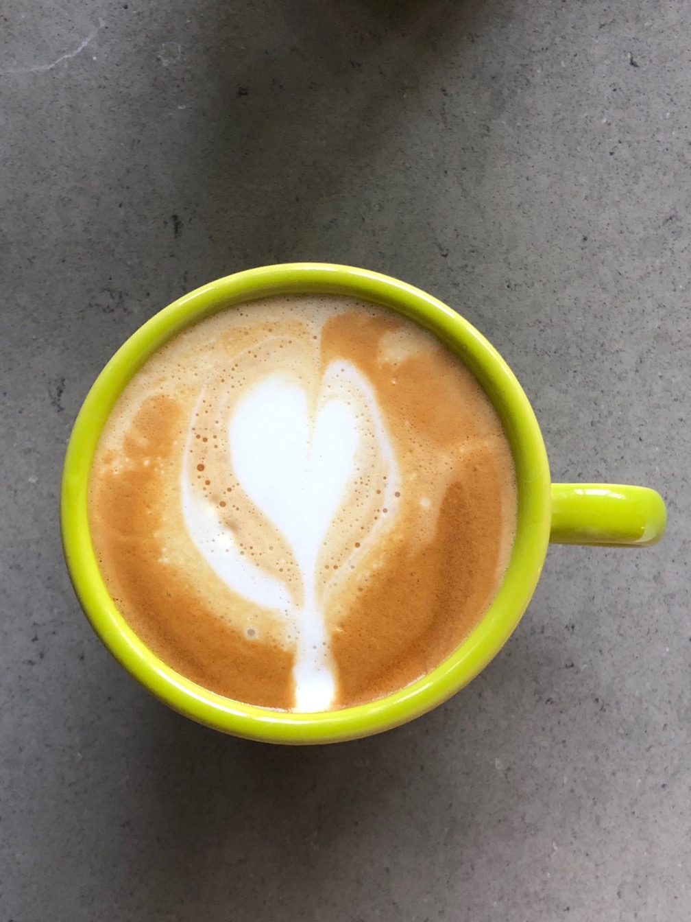 A photo of a cappuccino in a yellow cup, with a heart poured in the foam.  