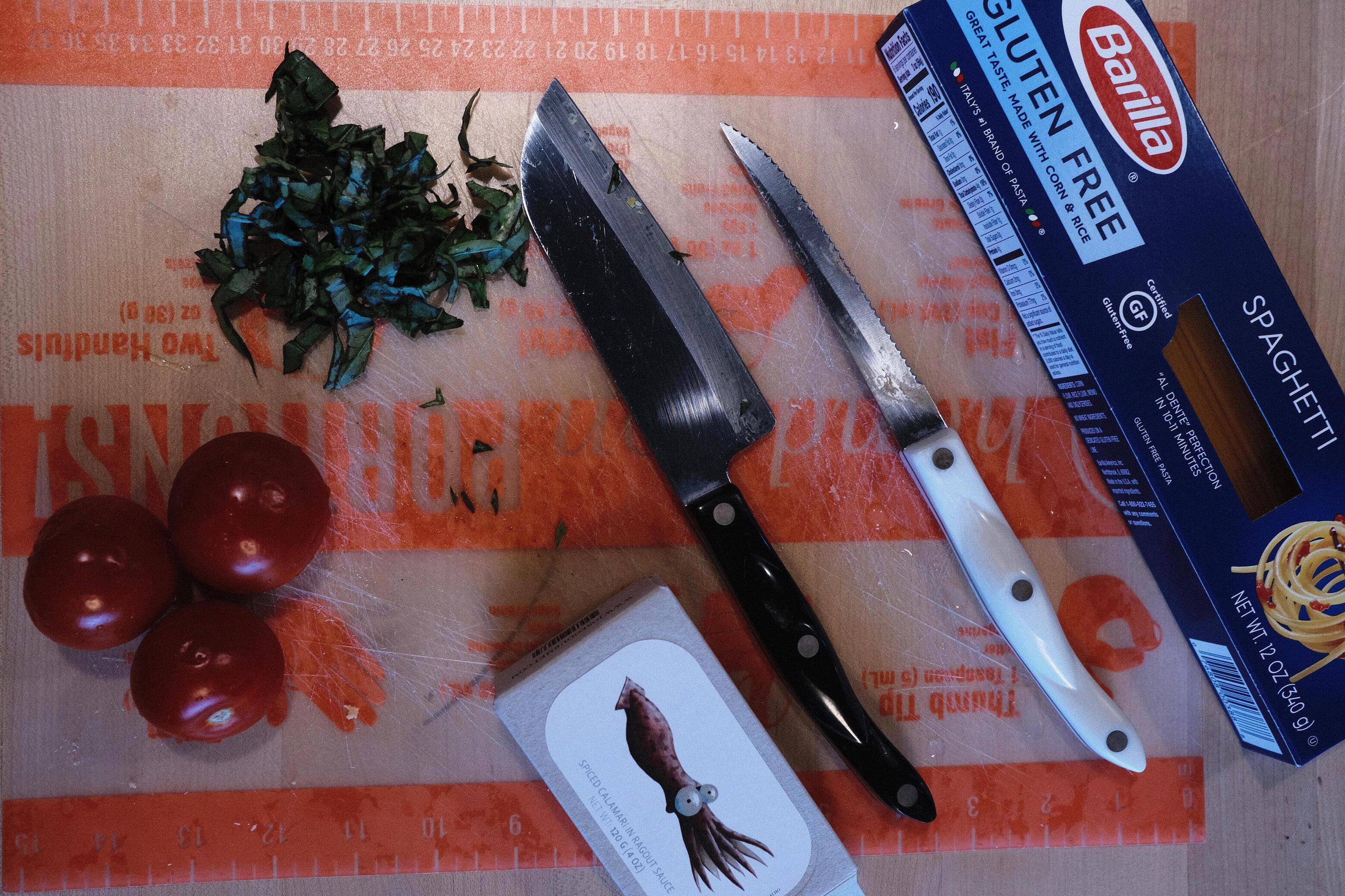 Photo of a cutting board with tomatoes, basil, spaghetti and a box of calamari 