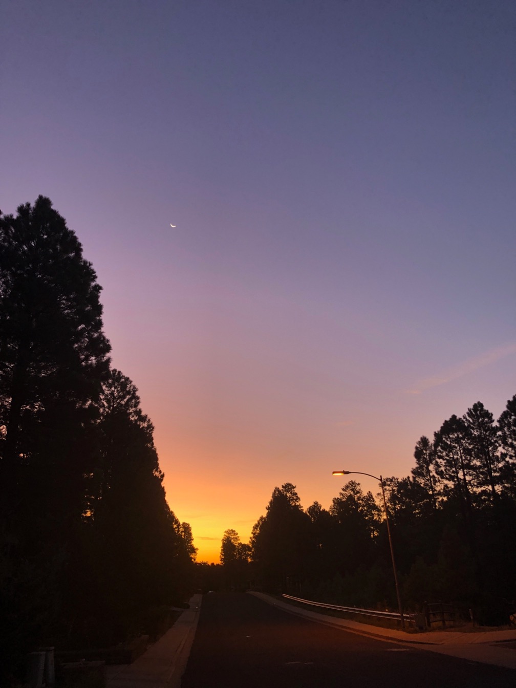 Photo of an orange and purple sunrise with tiny sliver of moon.  