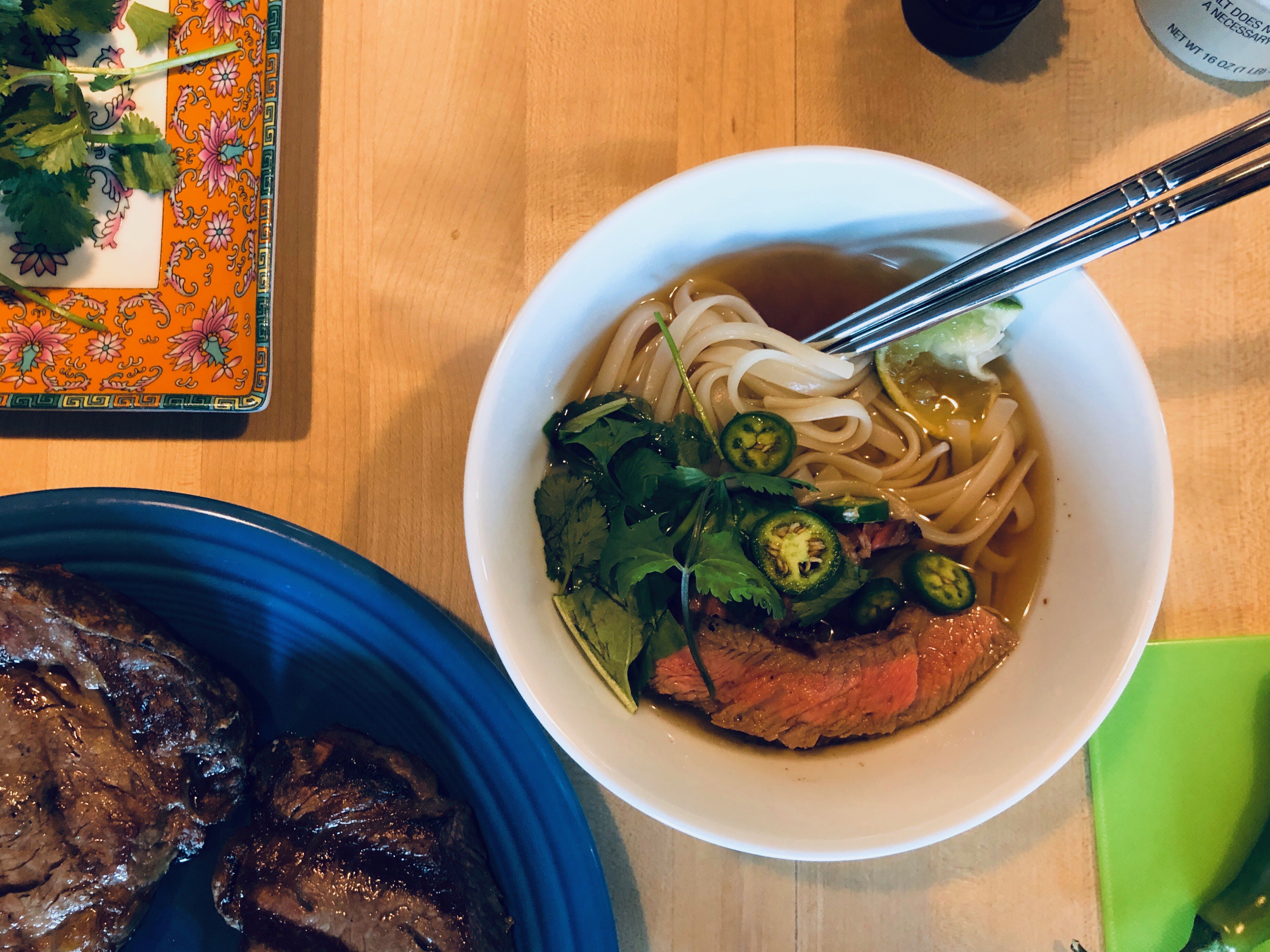 Photo of a bowl of dark brown broth with noodles, steak and cilantro 