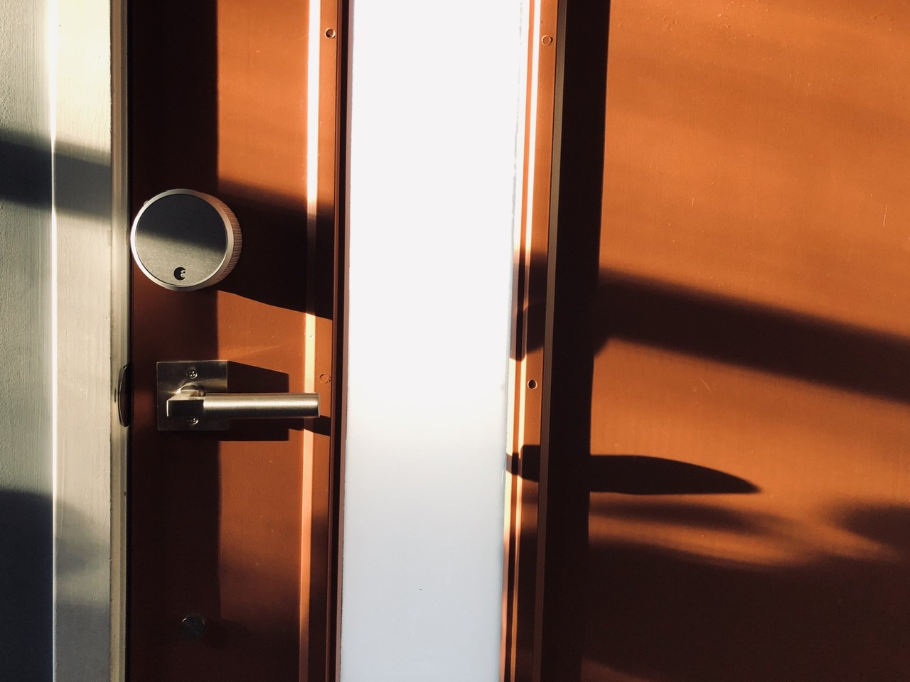 Photo of an orange door with an opaque window and crossed by diagonal shadows 