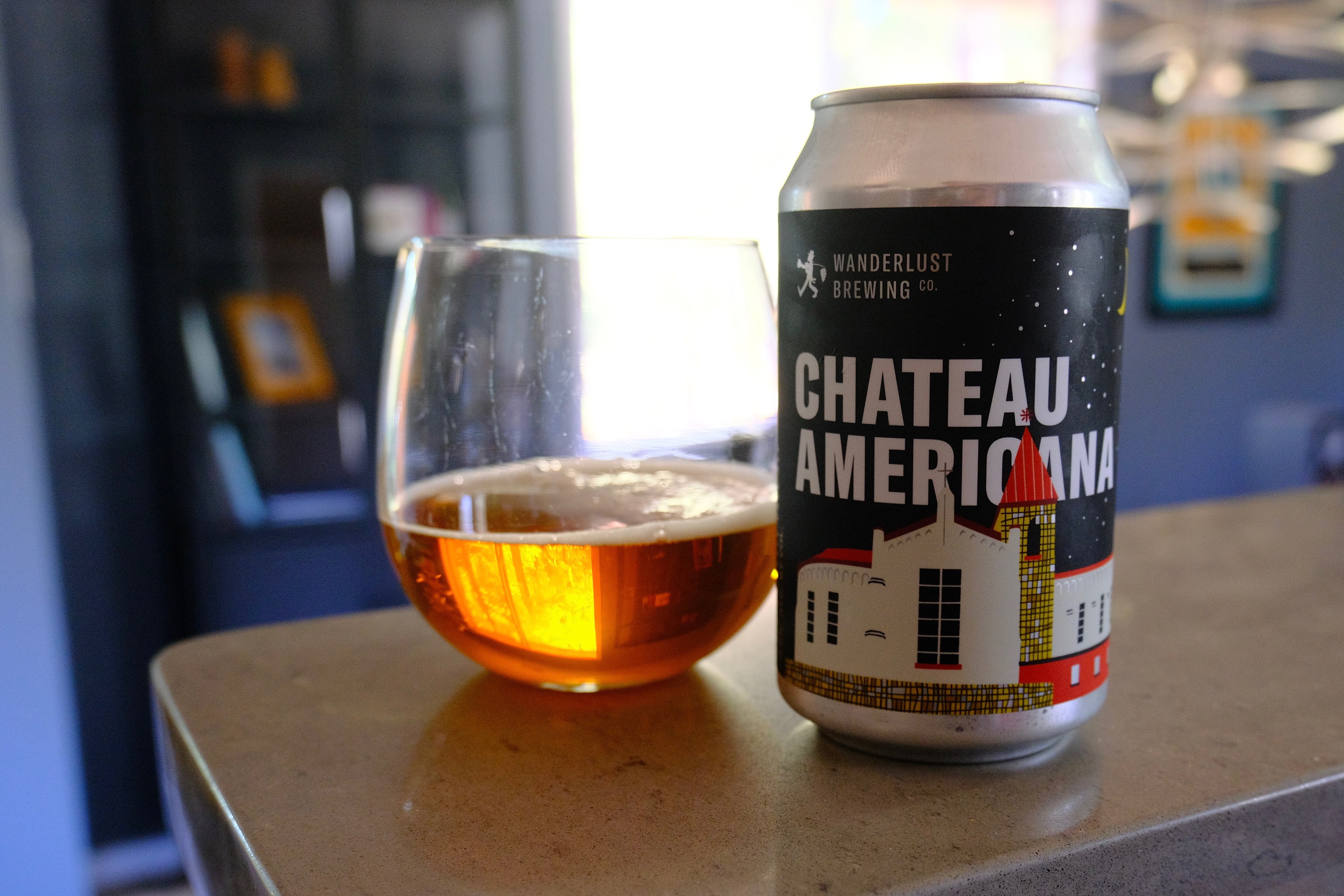 A beer glass half full, next to a can reading Chateau Americana 