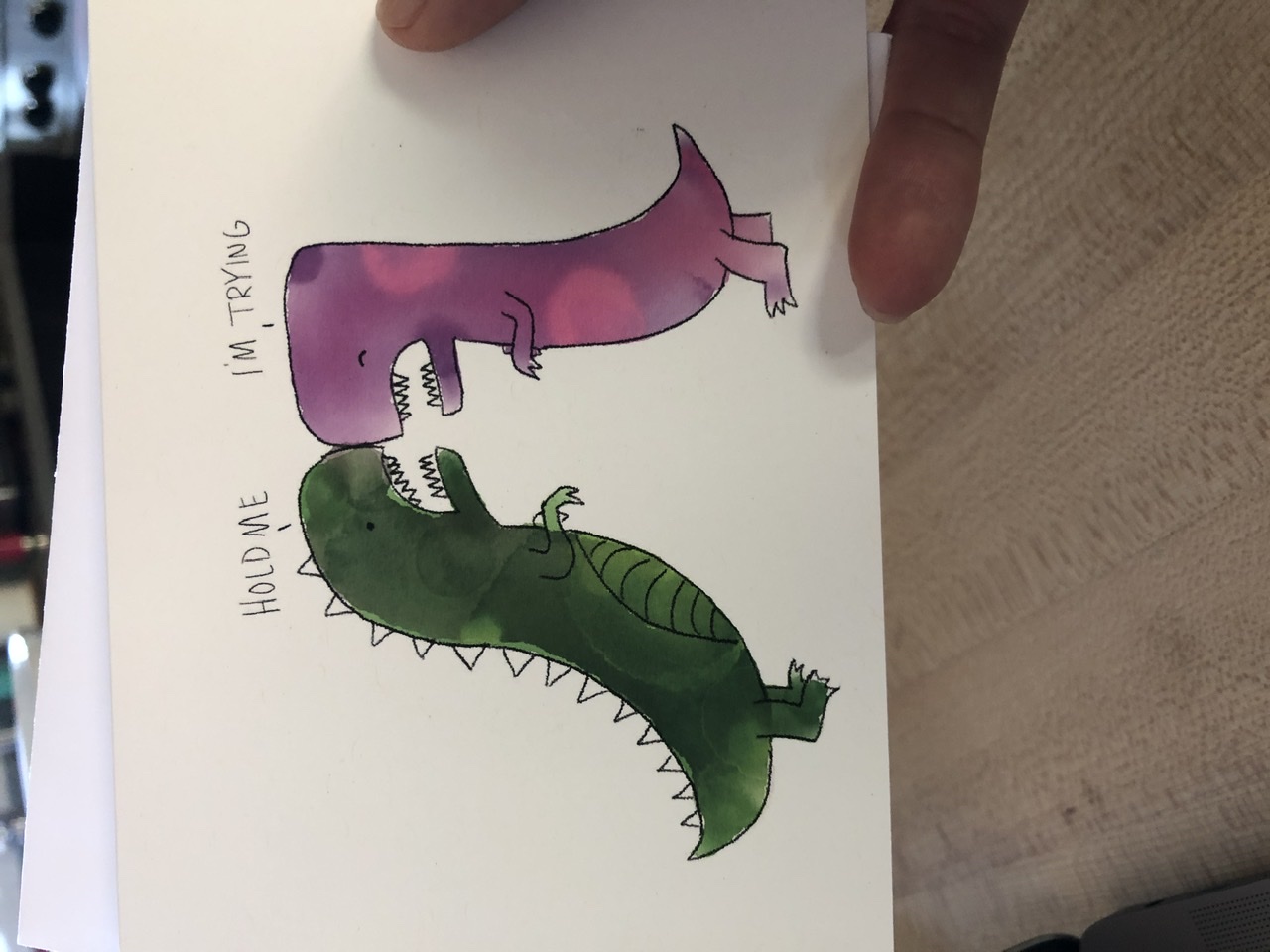 A greeting card showing two tiny armed dinosaurs trying to hug 