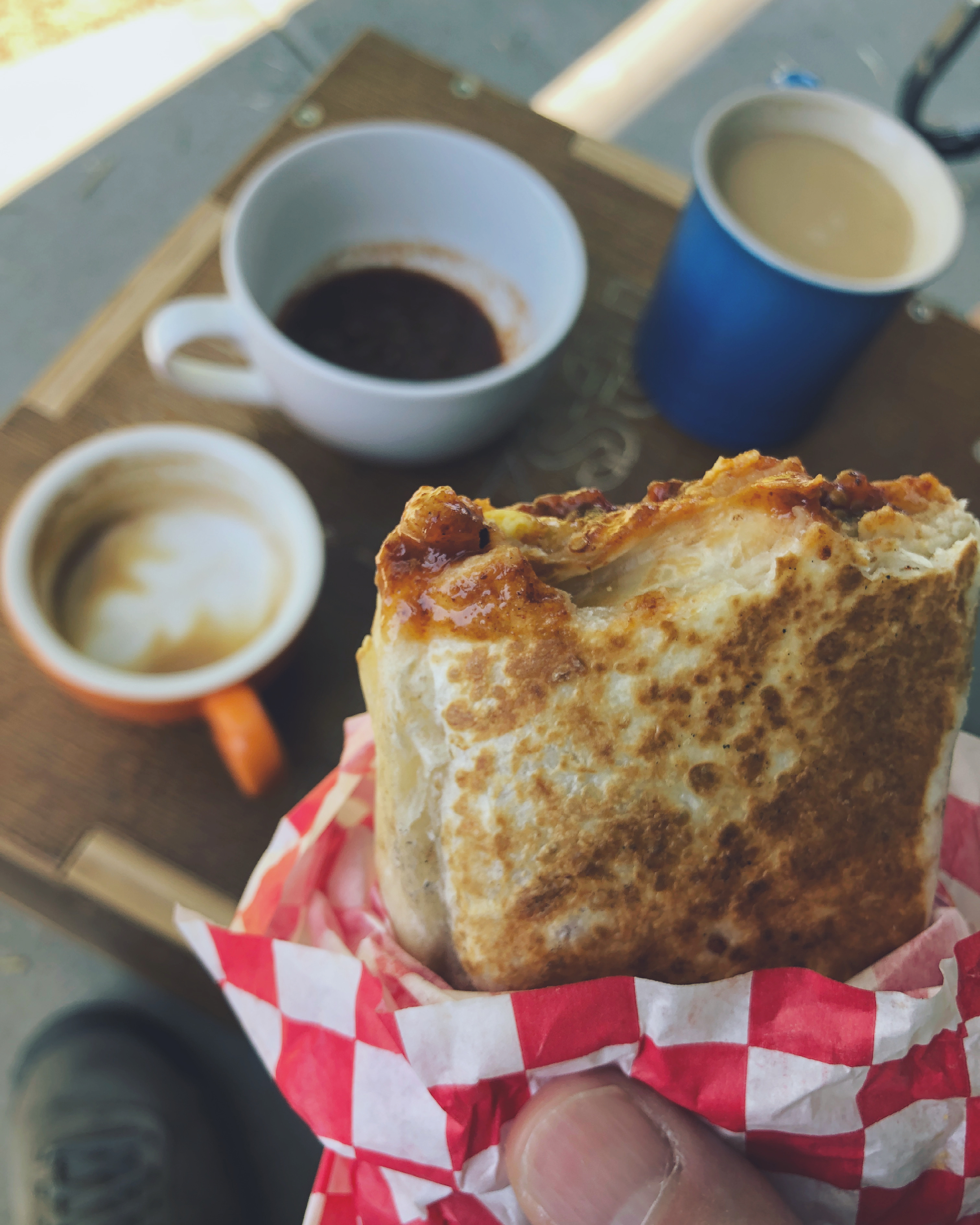 a breakfast burrito with golden brown toasting, held above a table with coffee and salsa 