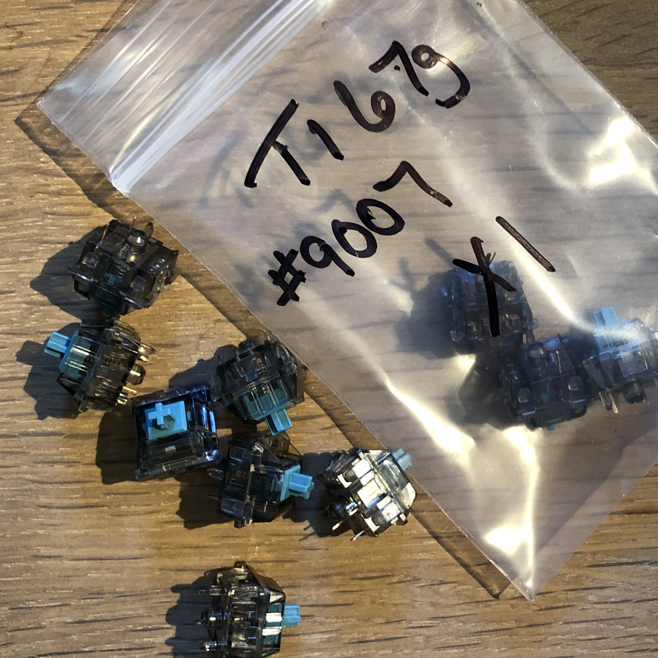 A plastic bag containing grey and blue keyboard switches. The bag is labeled T167g. 