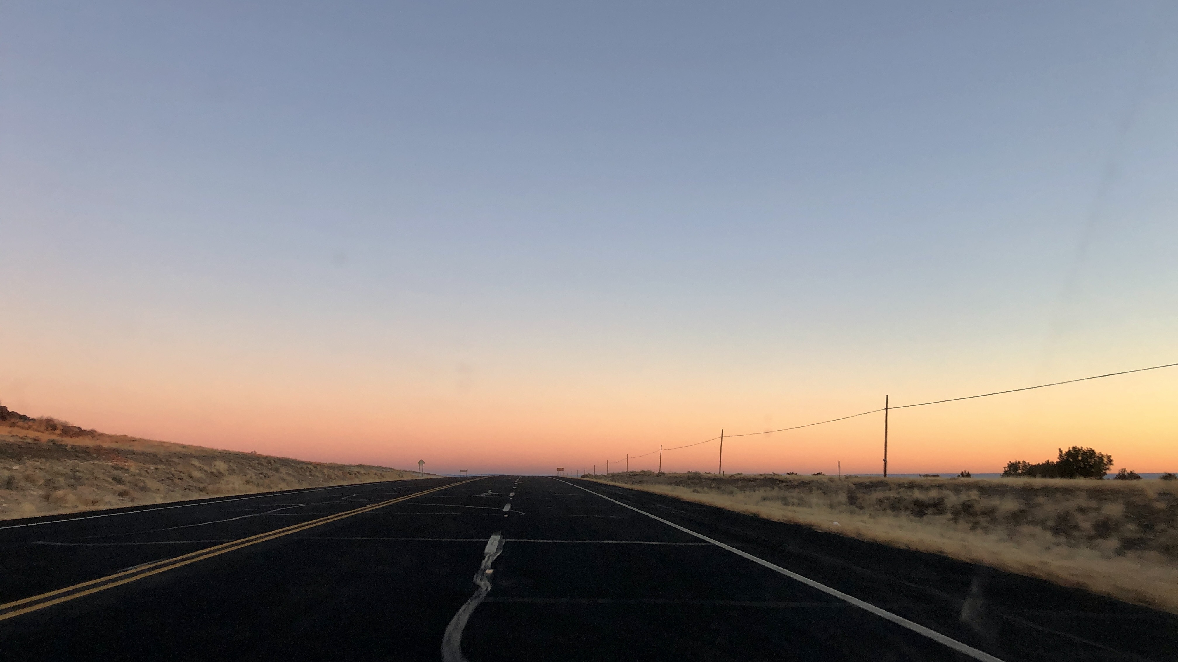 A dark road leading to a horizon lit by sunrise colored orange and blue 