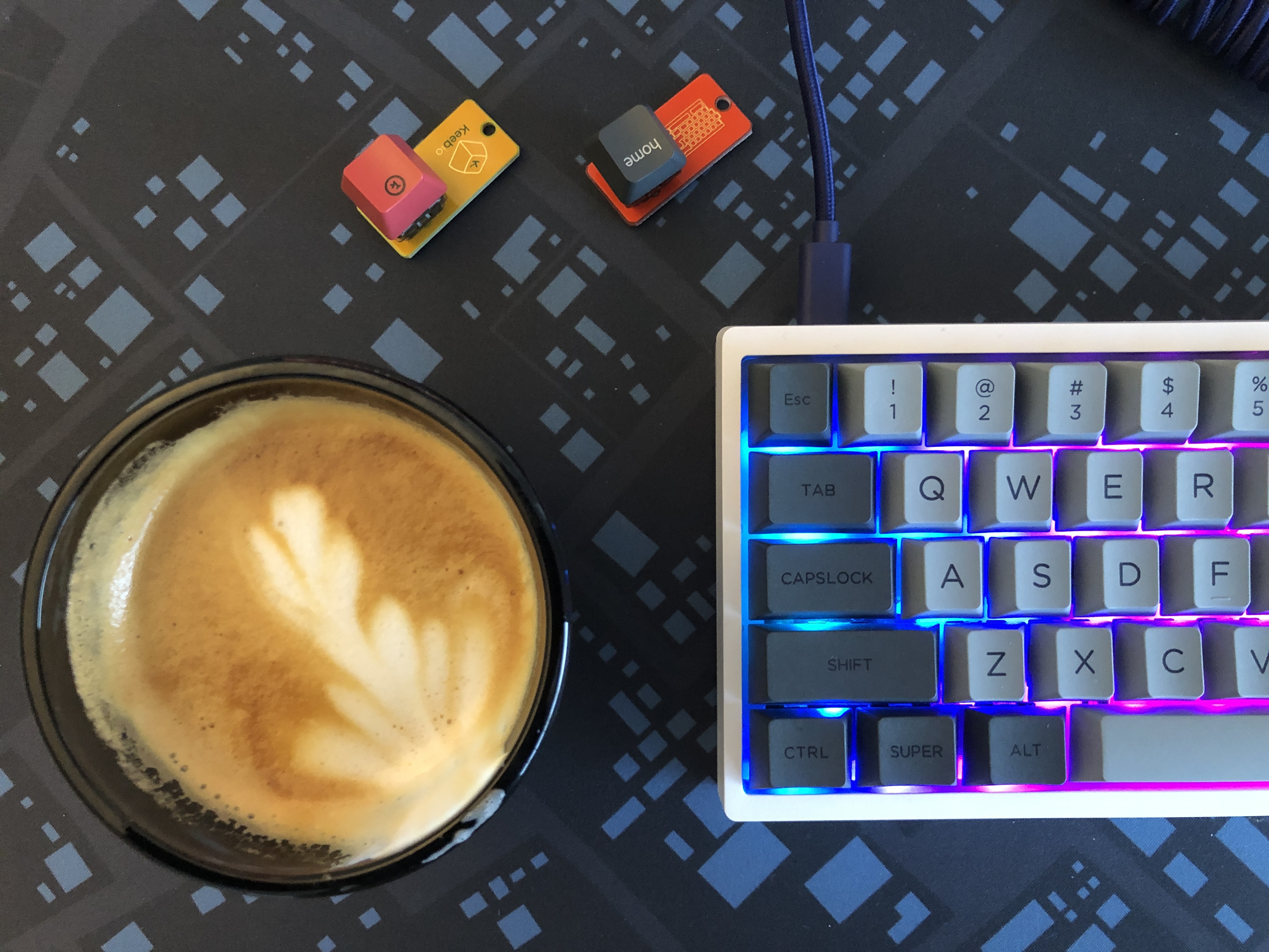 A cappuccino in a gray cup beside a colorfully-lit keyboard