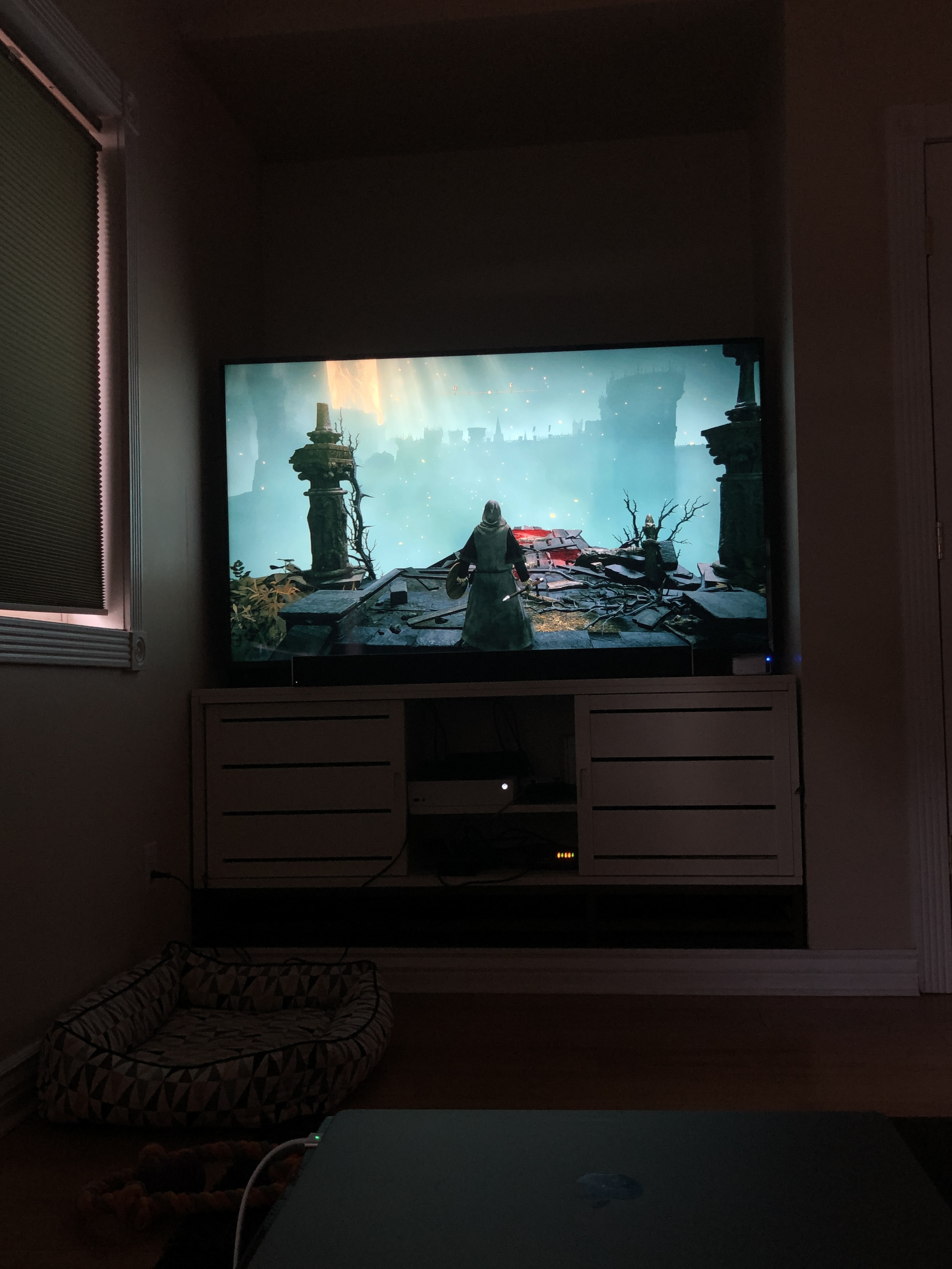 A TV in a dark room showing a video game character standing on a high platform overlooking a valley