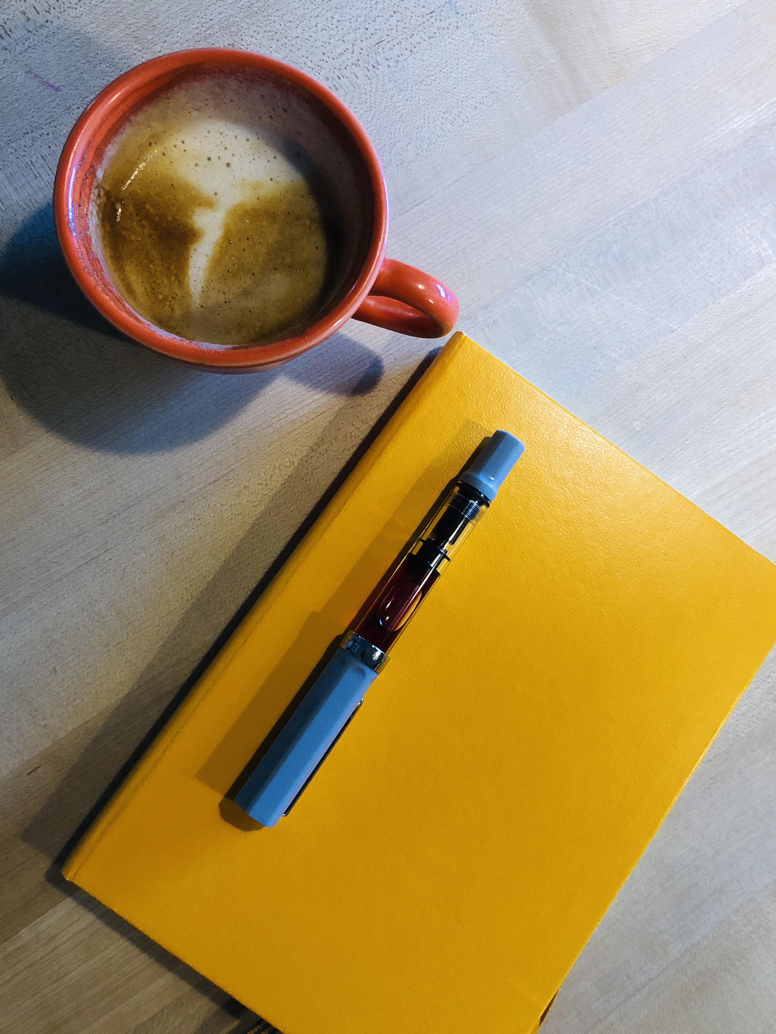 An orange coffee mug beside orange notebook and orange pen