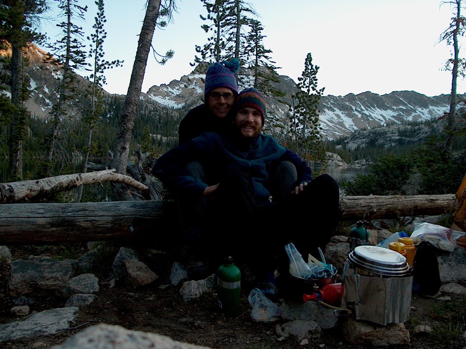 A man and woman sitting on a log beside a backpacking stove