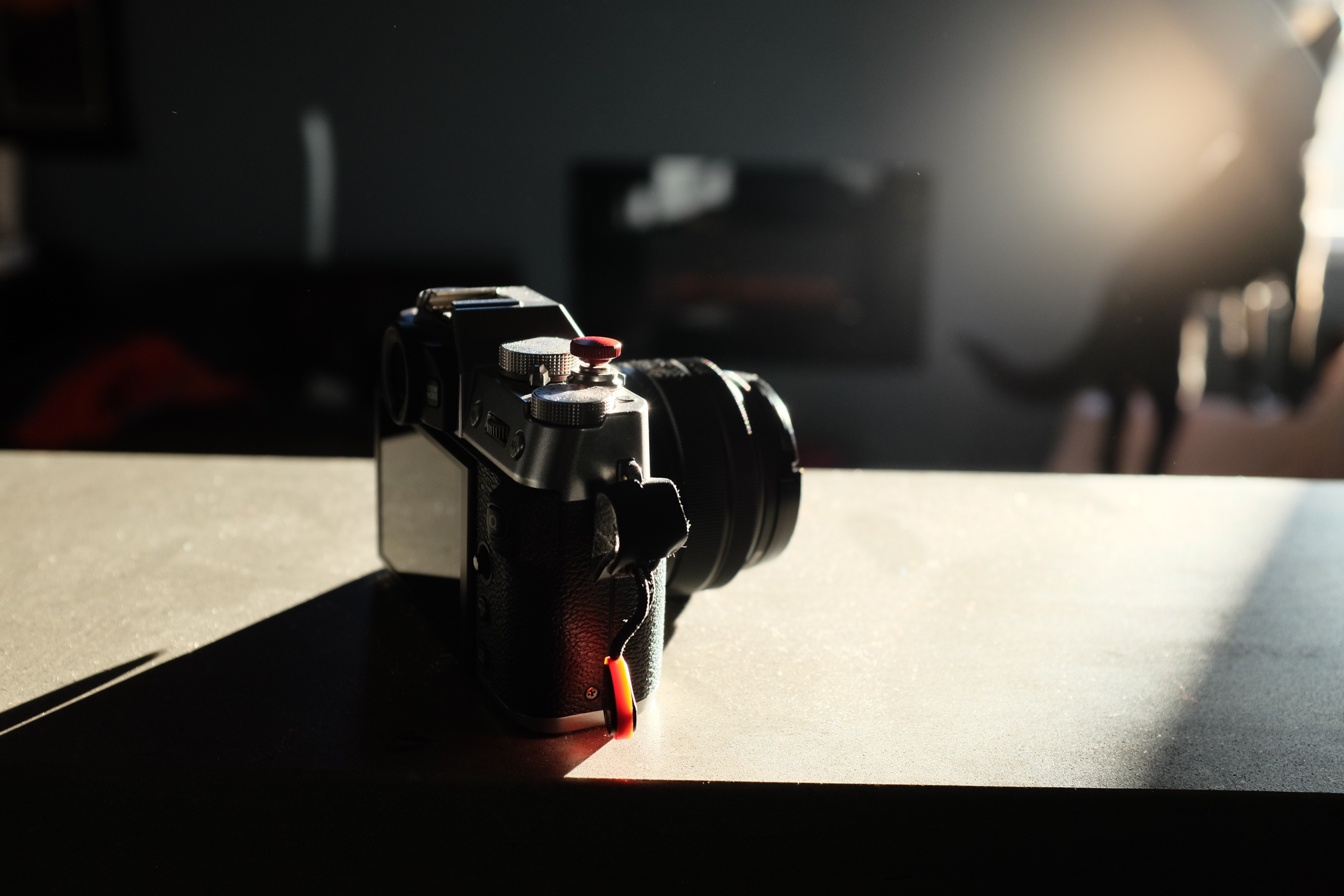 A silver and black camera sits on a bright, narrow countertop, lens pointing away. The light is bright, making the shadow very stark and deep behind the camera.