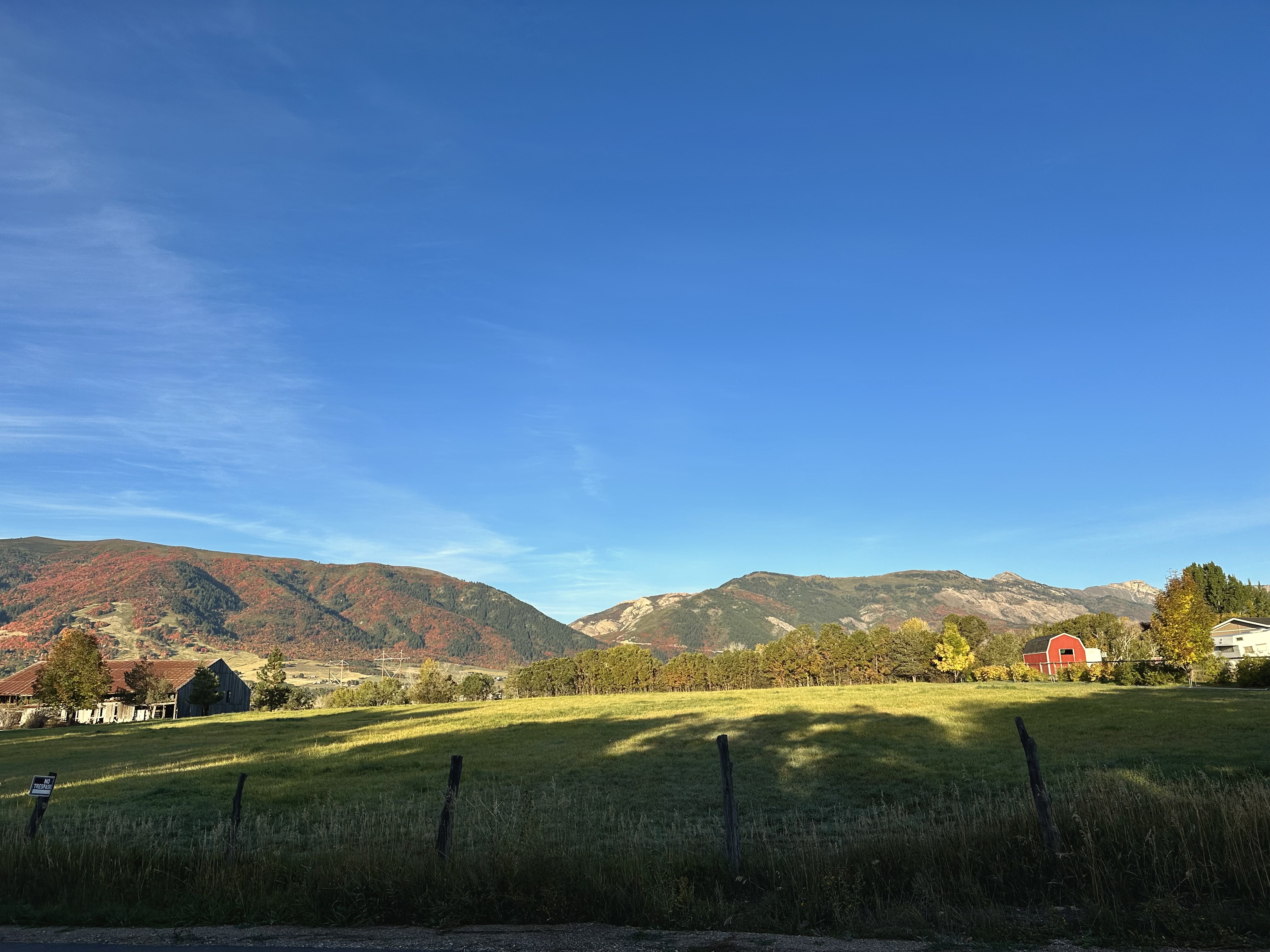 A mostly green pasture with a ridge of mountains beyond it. The ridge is streaked with red and orange fall colors.